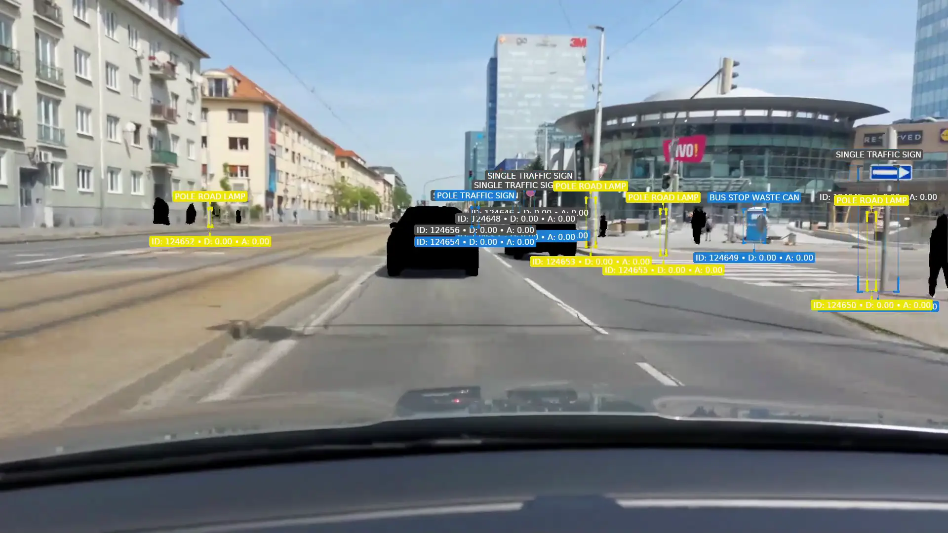 Jazda mestskou ulicou v Bratislave z kamery vozidla, s dopravnými značkami, stĺpmi, stromami a zastávkou, ktoré označila konzola CAMAN; vozidlá a ľudia sú začiernení