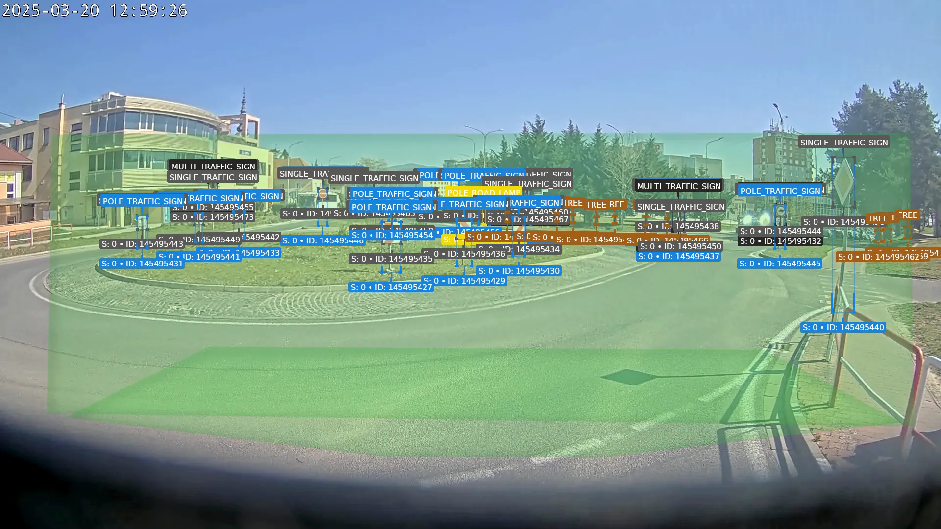 A vehicle’s camera going round a roundabout in Nové Mesto nad Váhom, the traffic signs, street lamps and trees labelled by the CAMAN console as they pass, then an alert on graffiti